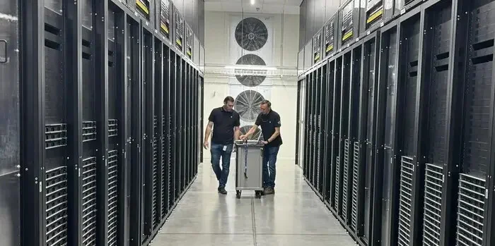 Illustrative server aisle with equipment racks and technicians moving a trolley