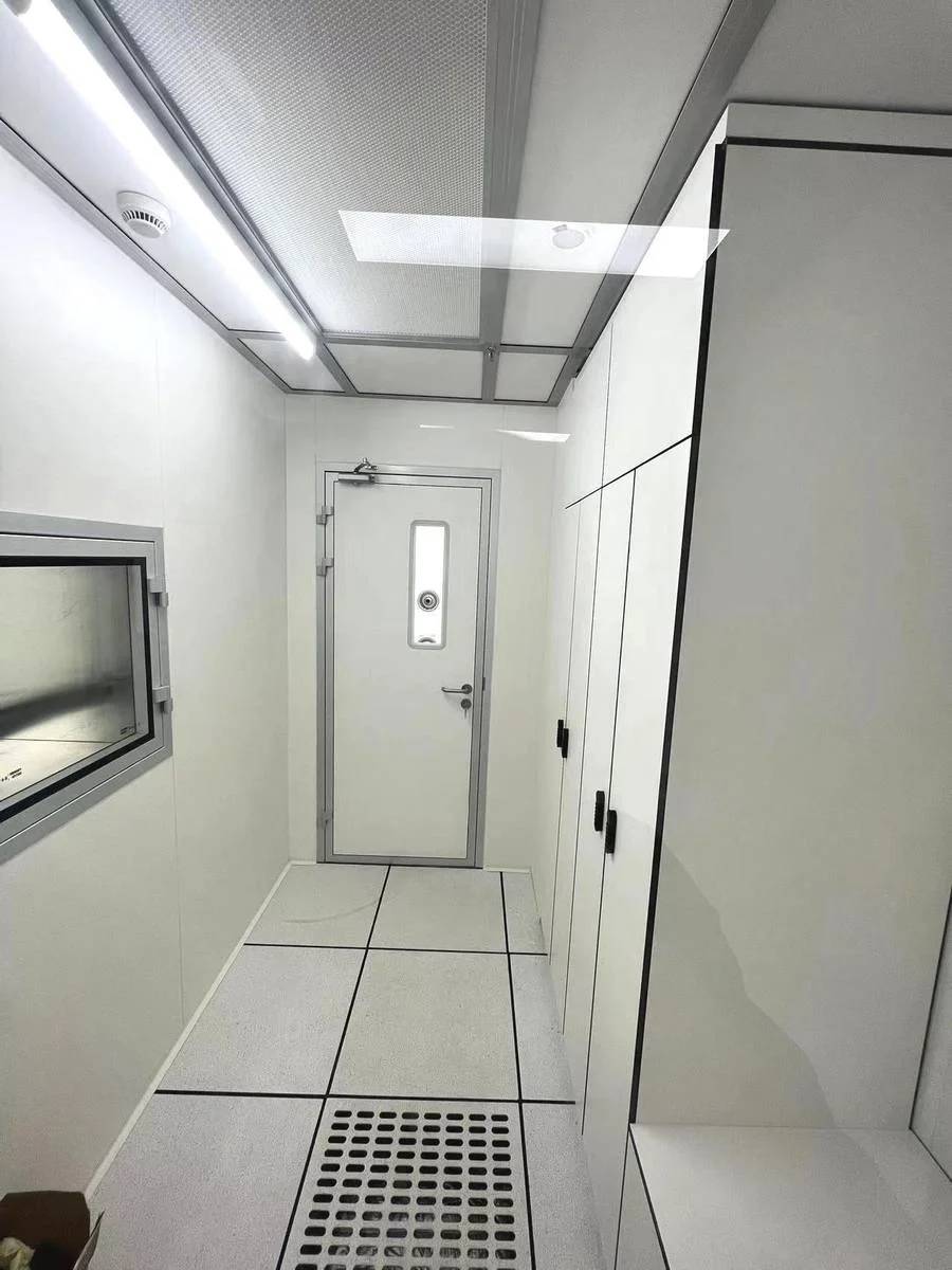 Pharmaceutical cleanroom corridor with flush prefabricated wall panels, a sealed cleanroom door and an integrated transfer window, forming part of a pressure-cascade layout